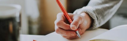 Person holding a pen and writing in an open notebook on a table.