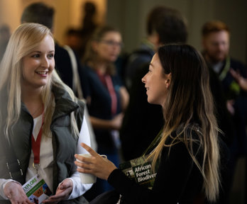 Two people at a conference smiling whilst engaged in a lively conversation.