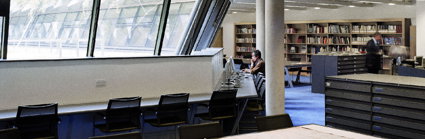 One person sits before a computer whilst the other looks at books on a shelf in in the Foyle reading room.