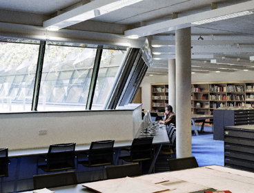 One person sits before a computer whilst the other looks at books on a shelf in in the Foyle reading room.