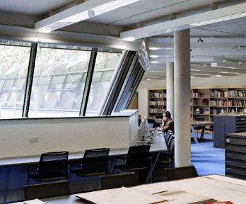 One person sits before a computer whilst the other looks at books on a shelf in in the Foyle reading room.