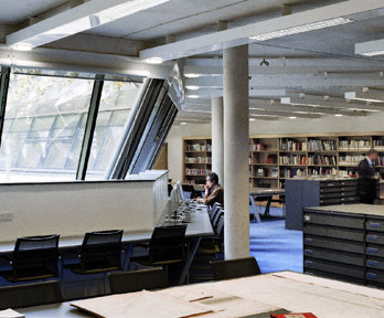 One person sits before a computer whilst the other looks at books on a shelf in in the Foyle reading room.