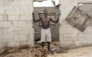 A local resident on the beach of Fuvemeh, Ghana, posing in the doorless doorway of a building affected by coastal erosion.