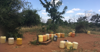 A cluster of water containers next to a well on a dirt path. 