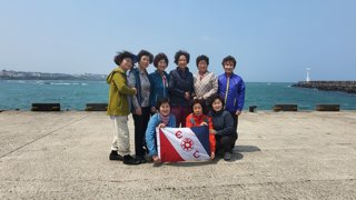 Nine people stand for a photo behind the Explorers Club flag at the side of a harbour with the sea behind them.