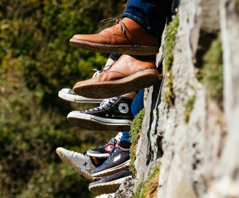 A group of people sitting on a wall but you can only see their feet dangling over the side.