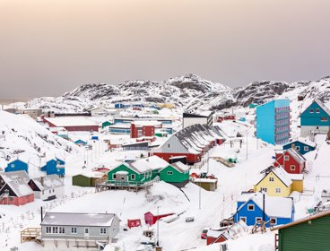 A view over a town in Greenland with colourful housing and snow covered ground and mountains