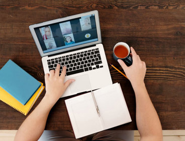 Overhead view of person working at desk with laptop and notebooks during video call. 