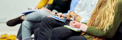 People sat with notebooks listening to a presentation and taking notes.