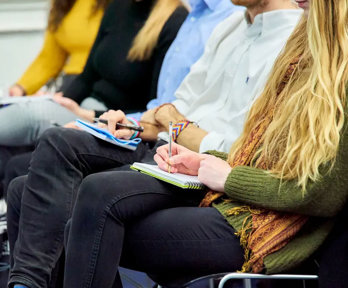 People sat with notebooks listening to a presentation and taking notes.