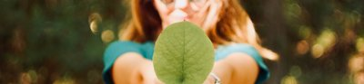 A woman hodling a green leaf out to the camera
