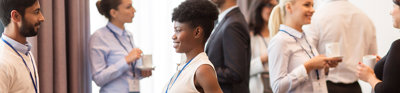 Business people with conference badges and coffee chatting with each other in a brightly lit room.