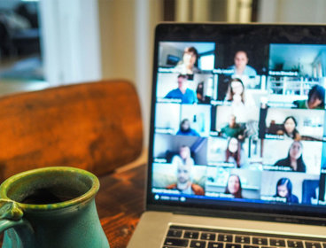 A cup next to a laptop with a blurry screen showing different people who are in an online meeting. 