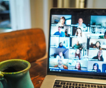 A cup next to a laptop with a blurry screen showing different people who are in an online meeting. 