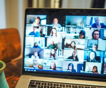 A cup next to a laptop with a blurry screen showing different people who are in an online meeting. 