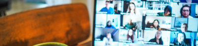 A cup next to a laptop with a blurry screen showing different people who are in an online meeting. 