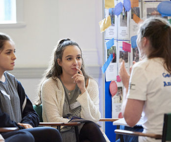 Two students listening attentively to a third person who's wearing a T-shirt with the text Geography Ambassador.