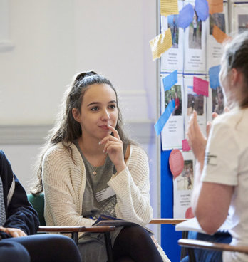 Two students listening attentively to a third person who's wearing a T-shirt with the text Geography Ambassador.