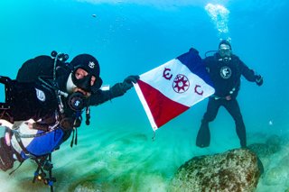 Two divers holding the flag of the Explorers' Club.