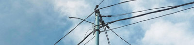 Electric post with cables under blue, partially cloudy sky.