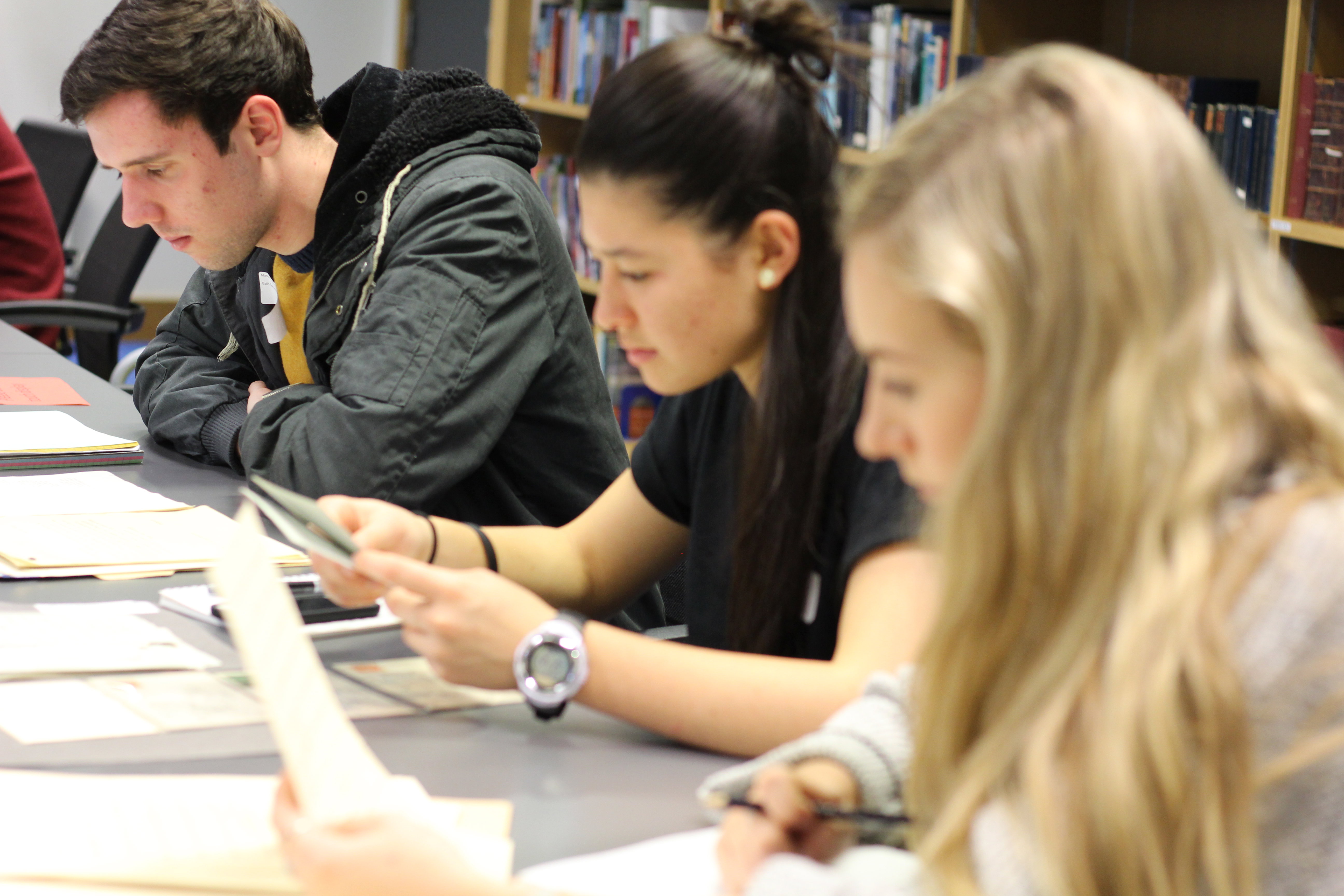 Three people sat at a table in a library, looking at paperwork.