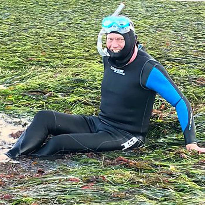 Tom Heap sitting on a bed of seagrass, wearing a wetsuit and snorkel set