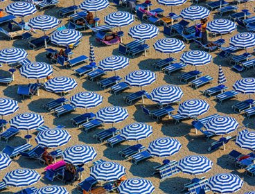 An aerial view of blue and white parasols and sun loungers on a sandy beach