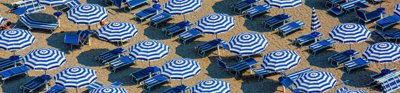 An aerial view of blue and white parasols and sun loungers on a sandy beach