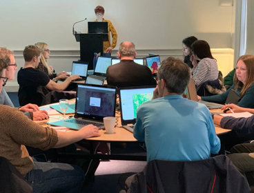 A group of teachers sit around a table with their laptops. They are using ArcGIS.