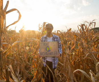 Person standing in crop field with sign saying 'There is no planet b'