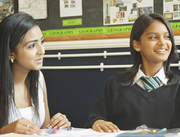 A student and teacher sitting together at a desk, looking at school work.