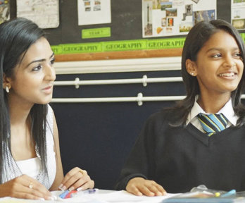 A student and teacher sitting together at a desk, looking at school work.