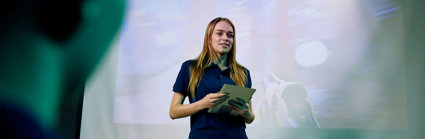 A person standing in front of a projection screen presenting to an audience.