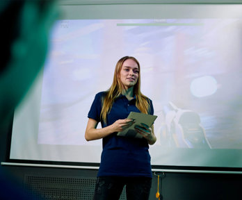 A person standing in front of a projection screen presenting to an audience.