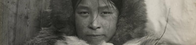 Black and white photo of an Inuit woman called Aqattaq. Aqattaq stares forward with a nutural expression wearing a fur top and fur hood.