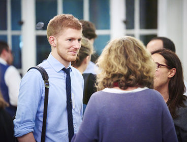 Man in a blue shirt and tie talking to two women