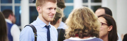 Person in a blue shirt and tie talking to two other people.