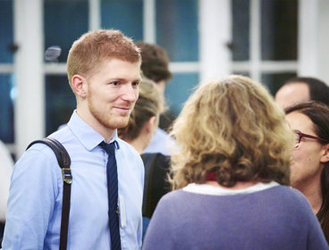 Person in a blue shirt and tie talking to two other people.