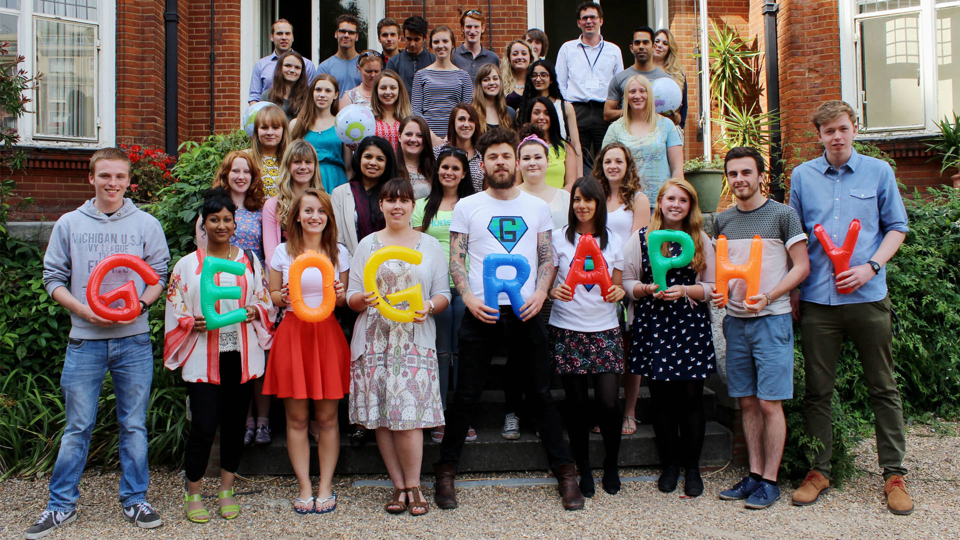 Group photo taken on the steps of the patio at the Society. The people in the front row each hold a letter, which together spell the word geography.