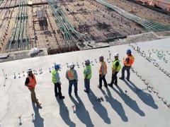 A group of people in high vis jackets standing on a roof top overlooking a building site