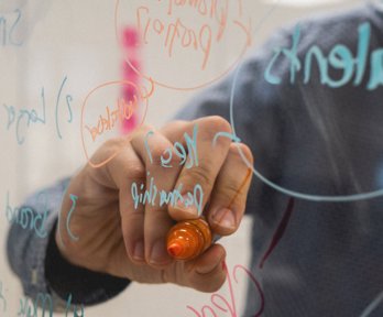 Person writing on a glass board with a felt-tip pen. 