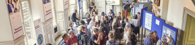 A group of people wearing lanyards in a stately Main Hall. The room features display boards and posters.