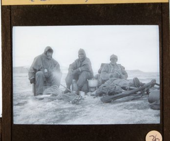 Historic black and white lantern slide showing three men wearing expedition clothing and with expedition equipment