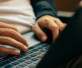 Person typing on a laptop which is resting on their lap.