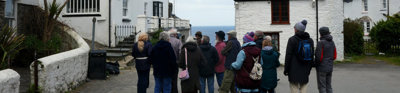 A tour group listening to the leader speaking in front of white, traditional seaside cottages.