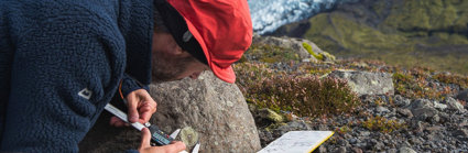 Person measuring the size of a mark on the side of a rock in a rocky landscape.