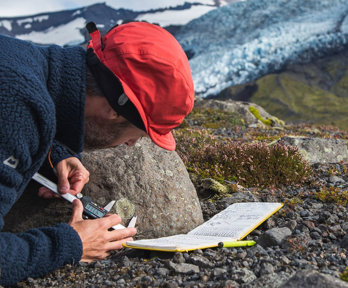 Person measuring the size of a mark on the side of a rock in a rocky landscape.