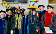 Seven people stood wearing graduation gowns and caps posing for picture.