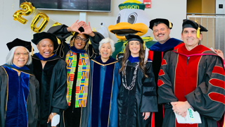 Seven people stood wearing graduation gowns and caps posing for picture.