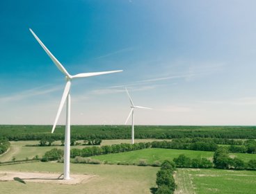 Two wind turbines in open fields with a clear sky. 